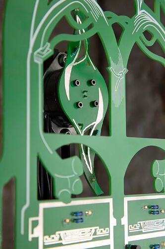 Slack Storage, right cabinet. Close-up of a green circuit board cut into an arched, leaf-like shape and covered in fine white line-work, with four metal mounting holes and a few small components. A black cooling fan is visible through the cut-outs behind it.